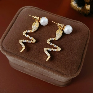 Macro detail of snake-shaped gold earring with zircon pave and white pearl on velvet