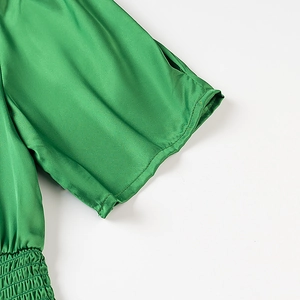 Detail of green satin top featuring elastic smocking texture and glossy finish