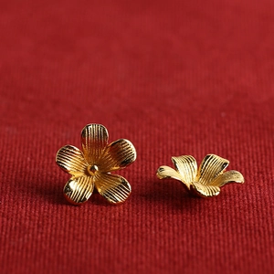 Golden five-petal flower stud earrings with brushed texture on red background