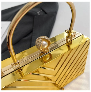 Macro detail of golden evening bag with V-shaped texture and pearl diamond clasp