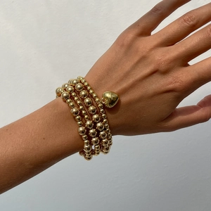 Detail shot of multi-layer gold beaded bracelet set with heart charm on female wrist