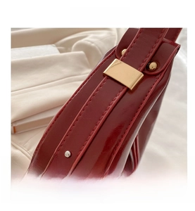 Close-up of burgundy patent leather underarm bag with gold metal buckle and stitching