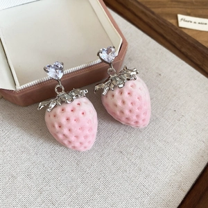 Detail of pink strawberry earrings with heart-shaped zircon studs on beige fabric