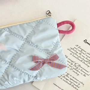 Detailed view of blue quilted makeup bag with pink zipper and striped ribbon bow detail