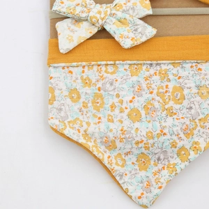 Close-up of baby cotton bib and headband set with yellow and grey floral print
