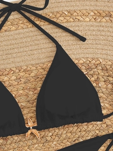 Macro detail of black bikini top with gold starfish charm on straw mat background