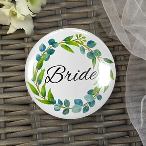 Close-up of white floral Bride tinplate badge for hen party on a grey woven surface