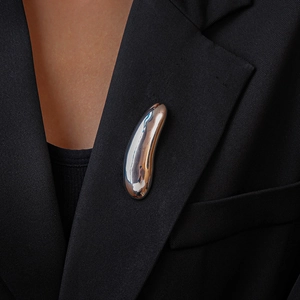 Close-up of a silver polished water drop brooch on a black blazer lapel, minimalist style