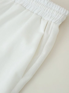 Detail of white cotton linen trousers featuring elastic waistband and side pocket seams