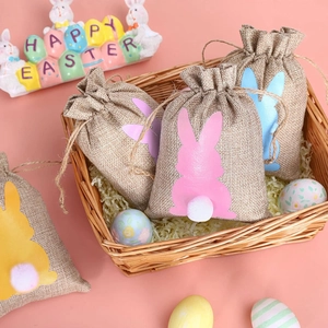 Close-up of Easter burlap gift bags with bunny tail pom-poms in a woven basket