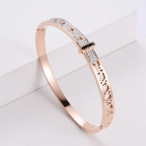 Rose gold geometric bangle with inset crystals and Roman numerals on white pedestal