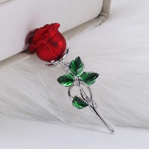 Elegante roosvormige broche van rood emaille met groene bladeren op pluche
