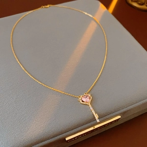 Detail of gold heart key pendant with pink zircon and rhinestones on a gray velvet box
