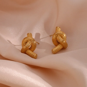 Close-up of golden knotted button stud earrings on soft pink silk fabric background