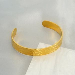 Macro shot of gold hammered stainless steel bangle on marble with luxury texture
