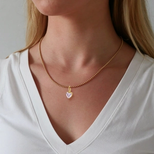 Close-up of a gold heart pendant with a sparkling zircon stone worn by a model