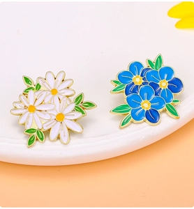 Detail of colorful daisy and blue flower enamel pins with gold trim on display stand