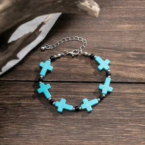 Detail of turquoise cross beaded bracelet with silver chain on dark wood background