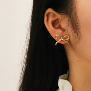 Close-up of gold bow earrings with a detailed twisted rope texture on a model