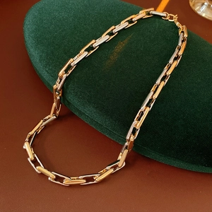 Macro detail of a two-tone gold and silver chain link necklace on a green velvet pad