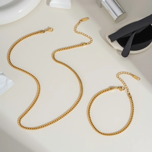 Classic golden stainless steel keel chain necklace and bracelet set on a plain surface