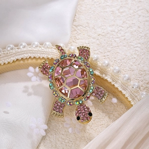 Detail shot of golden turtle brooch with pink gems and rhinestones on lace fabric