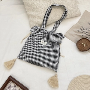 Detail of gingham tote bag featuring ruffle trim, side tassels, and a central fabric label