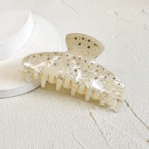 Detail of transparent rhinestone hair claw clip on white textured minimalist background