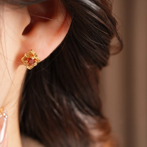 Close-up of vintage gold stud earring with deep red zircon stone on model ear