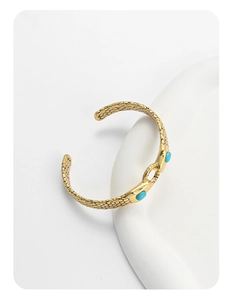 Detail of a gold snake-textured cuff bracelet with turquoise stones on white background