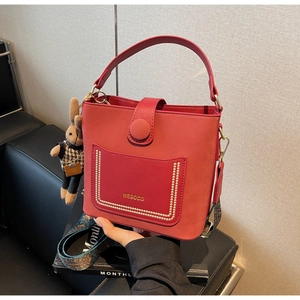 Detail view of red leather bucket bag with colorful wide strap and plush bunny charm