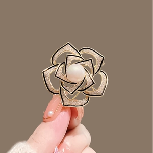 Macro shot of camellia brooch with matte gold petals, rhinestones, and center pearl