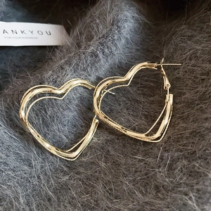 Close-up of golden double-layered heart-shaped earrings on grey faux fur texture
