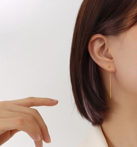 Close-up of a model wearing elegant gold drop earrings with minimalist long chain design