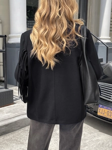 Close-up of elegant black jacket featuring decorative tassel details on long sleeves