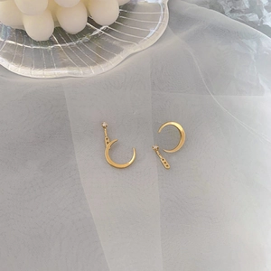 Détail de boucles d'oreilles lune dorées avec zircons sur un tissu en mesh blanc