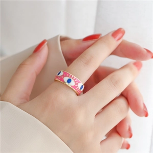 Detail of wide gold ring featuring pink enamel and evil eye patterns on a finger