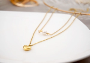 Close-up of double-layer gold heart necklace with white pearl on white ceramic plate