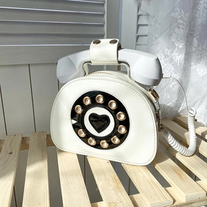 Creative white vintage telephone shaped shoulder bag with golden dial on wooden fence