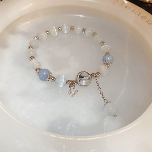 Detail of beaded bracelet with white cat-eye stones, blue beads, and star charms in a ceramic dish