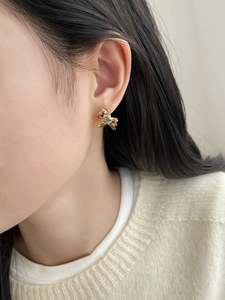 Close-up of a gold-plated earring with colorful gemstones worn on a female ear