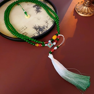 Detail of green beaded necklace with white tassel and cloisonne flower pendant