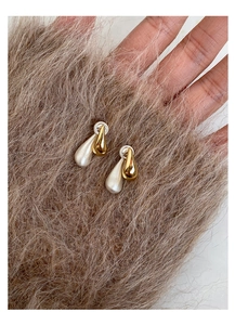 Detailed view of two-tone teardrop earrings held against a soft fur background