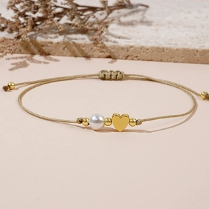 Detailed macro view of a gold braided bracelet with a pearl and heart charm