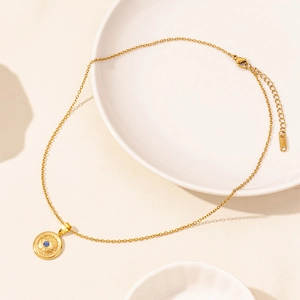 Gold stainless steel evil eye pendant necklace with blue gemstone on ceramic plate
