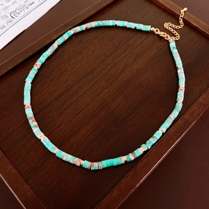 Detail of turquoise beaded necklace with gold spacers on a rustic dark wooden tray
