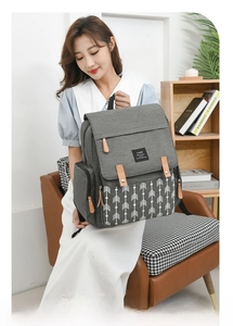 Detail view of a gray canvas diaper bag backpack with geometric arrow pattern and leather tabs