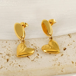 Macro detail of gold heart earrings with LOVE engraving on a satin and stone surface