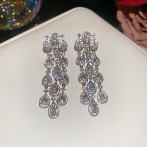 Close-up of sparkling silver tassel earrings with zircon flowers on white leather background