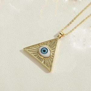Macro shot of gold-plated evil eye triangle pendant with realistic blue iris on metal chain